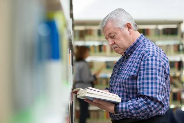 Старик читает и выбирает книгу в библиотеке — стоковое фото