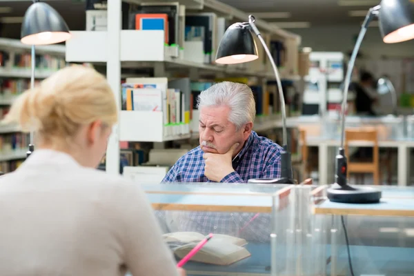 Äldre man studerar bland unga i biblioteket — Stockfoto