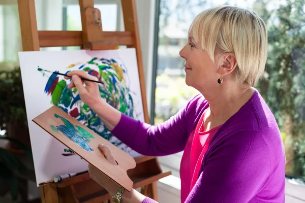 Счастливая пожилая женщина рисует для развлечения дома — стоковое фото
