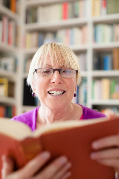 Szczęśliwa kobieta starszy okularach, czytanie książki w domu — Zdjęcie stockowe