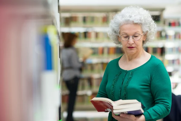 Mulher sênior lendo e escolhendo livro na biblioteca — Fotografia de Stock