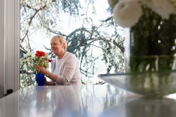Літня біла жінка з квітами вдома — стокове фото
