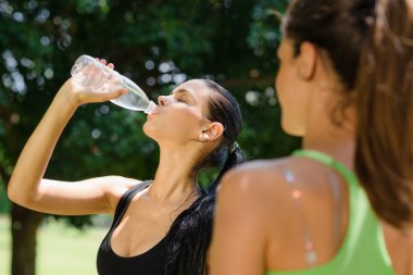 Two young women relaxing after fitness in park clipart