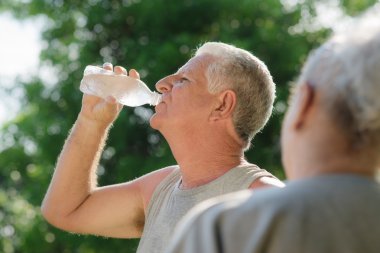 Seniors drinking water after fitness in park clipart