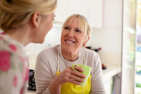 Mãe e filha conversando, bebendo café na cozinha — Fotografia de Stock