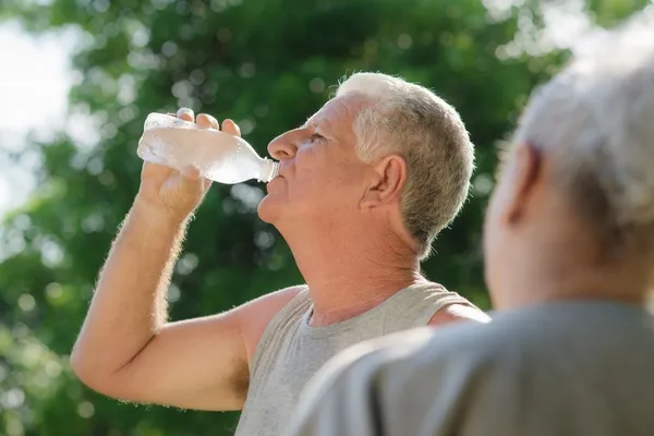 Пожилые люди пьют воду после фитнеса в парке — стоковое фото