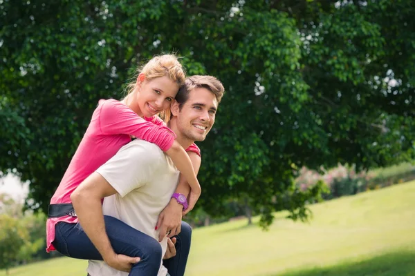 Young couple running piggyback in city park — Stock Photo, Image