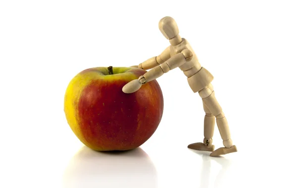 Wooden puppet pushing the apple — Stock Photo, Image