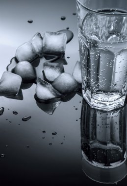 Glass of water and ice cubes on a dark background clipart