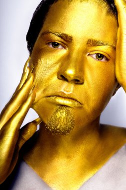 The boy's head painted with gold paint stares into the camera. clipart