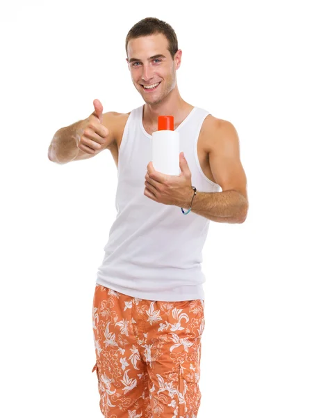 Happy young guy showing sun screen creme and thumbs up — Stock Photo, Image