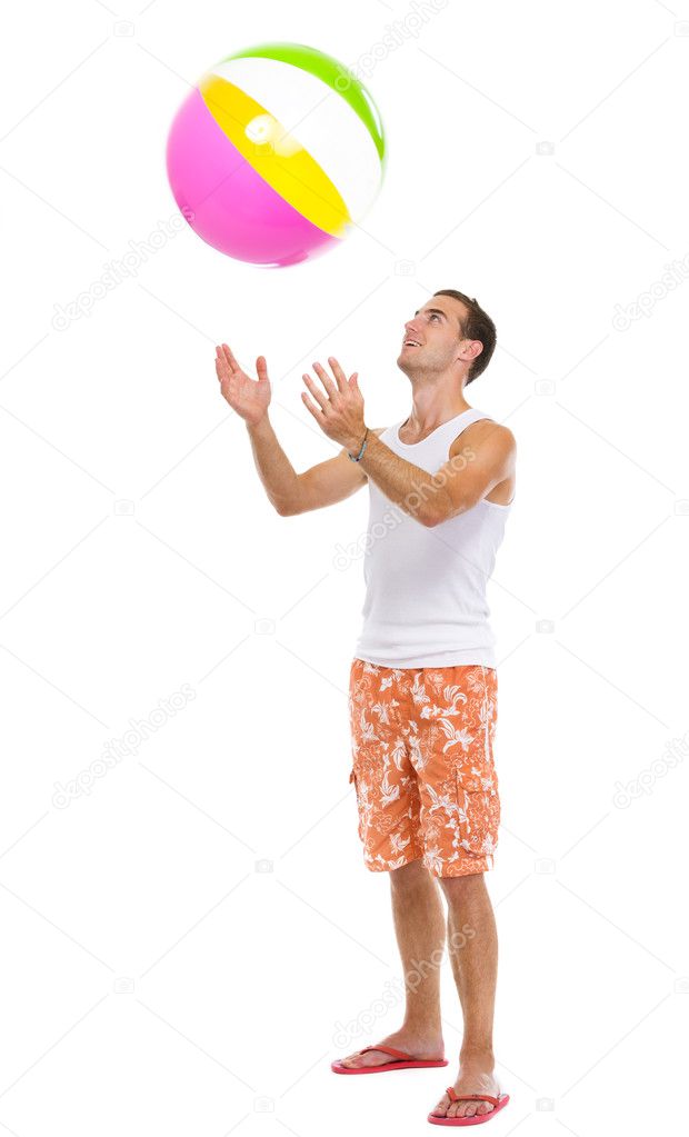Resting on vacation happy young man throwing beach ball up
