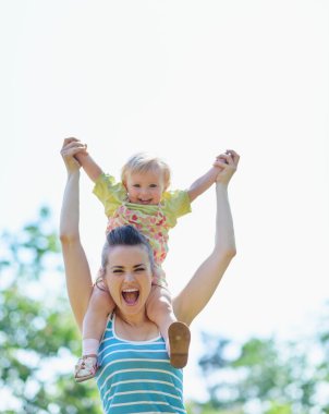 Happy mother with baby sitting on shoulders clipart