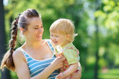 Happy mother tickling baby outside clipart