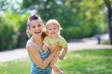 Smiling mother and baby playing in park clipart