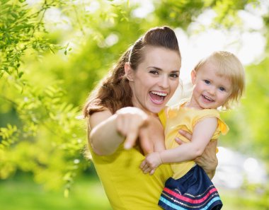 Portrait of baby girl and smiling mother pointing in camera clipart