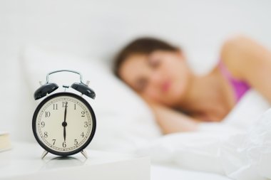 Alarm clock on table and woman sleeping in background clipart