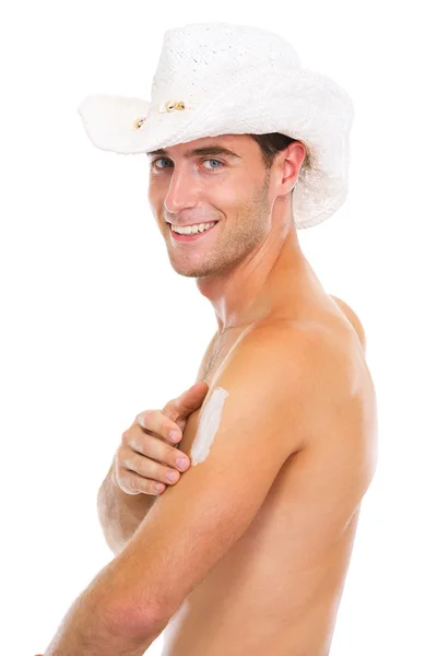 Smiling guy in hat applying sun block creme on arm — Stock Photo, Image
