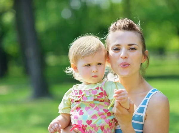 Junge Mutter und Baby pusten Löwenzahn weg — Stockfoto