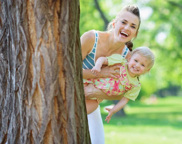 Smiling mother and baby looking out from tree — Stock Photo, Image