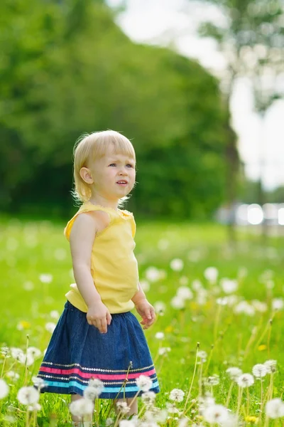 Baby girl on dandelions field looking on copy space — Stock Photo, Image
