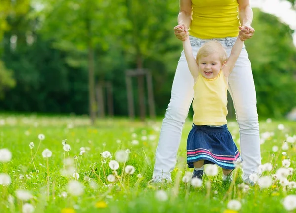 Mother playing with baby girl on dandelions field — Stock Photo, Image