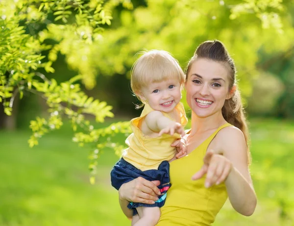 Portrait of baby girl and smiling mother pointing in camera — Stock Photo, Image
