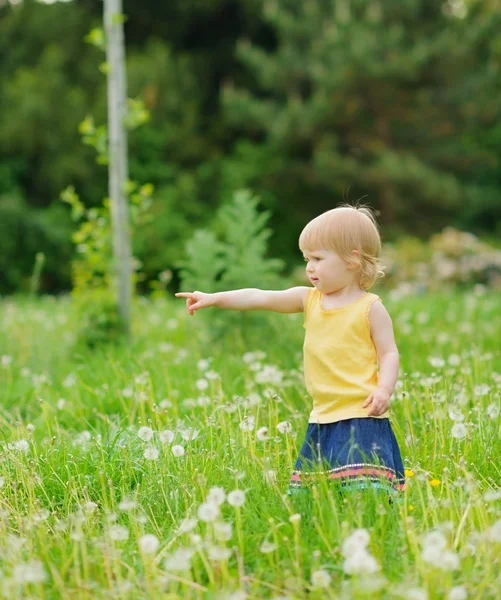 Baby girl on dandelions field pointing on copy space — Stock Photo, Image