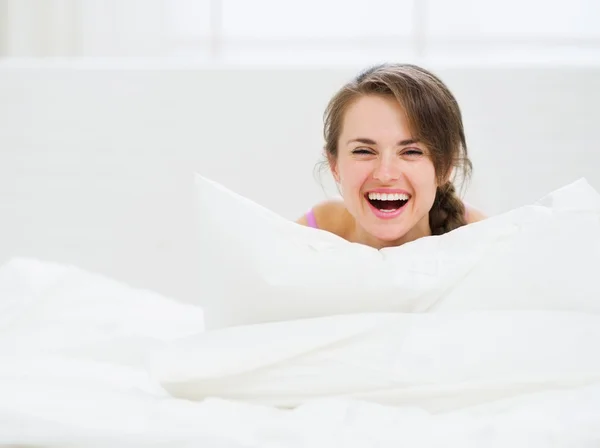 Χαμογελαστή γυναίκα βάζοντας στο κρεβάτι και να κρύβονται πίσω από το μαξιλάρι — Φωτογραφία Αρχείου