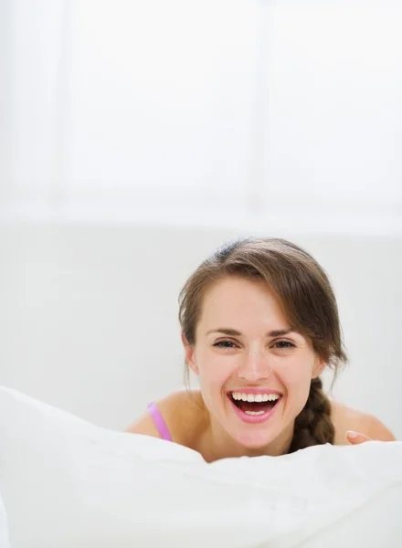 Lächelndes Mädchen liegt im Bett und versteckt sich hinter Kopfkissen — Stockfoto