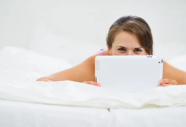 Улыбающаяся женщина лежит в постели и прячет планшетный компьютер — стоковое фото