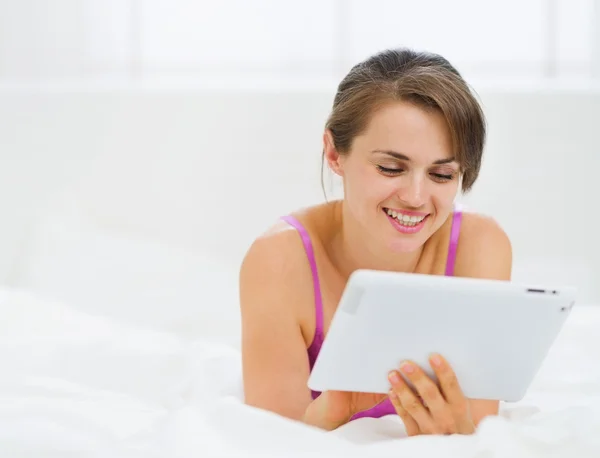 Lachende meisje tot in bed en de tablet pc gebruiken — Stockfoto
