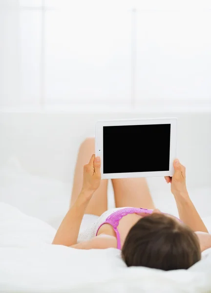 Женщина лежит в постели и держит планшетный компьютер — стоковое фото