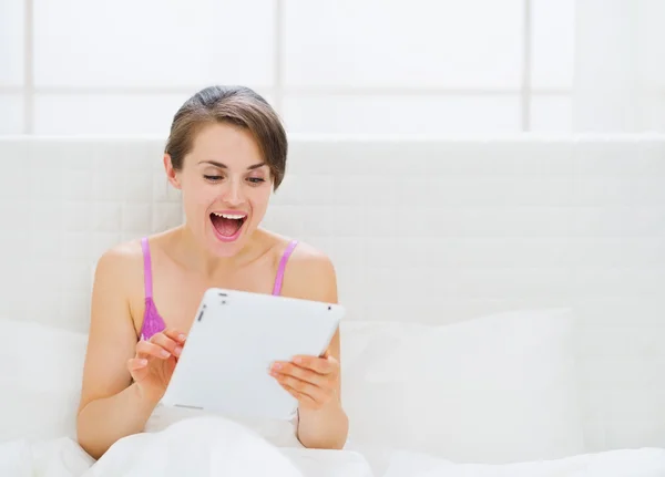 Zaskoczony kobieta siedzi na łóżku i przy użyciu komputera typu tablet — Zdjęcie stockowe