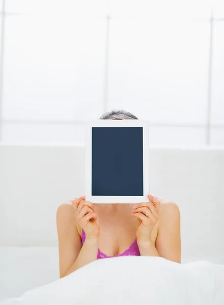 Chica sentada en la cama y escondiendo tableta PC en frente de la cara — Foto de Stock
