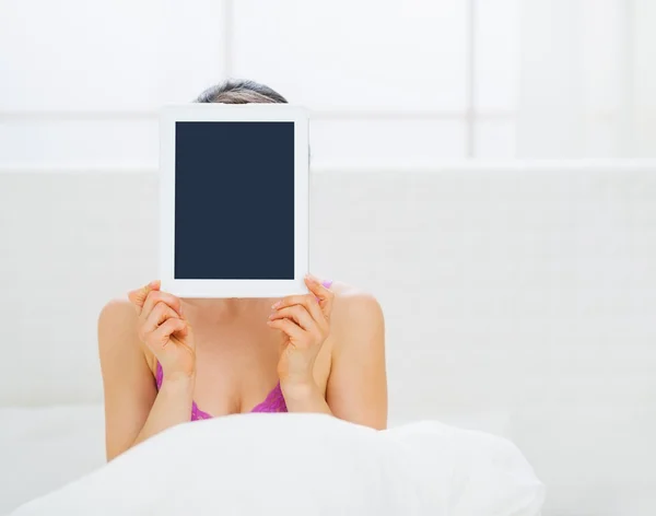 女性はベッドに座っていると顔の前でタブレット pc を隠す — ストック写真
