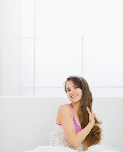 Glücklich schöne Frau mit langen Haaren sitzt im Bett — Stockfoto