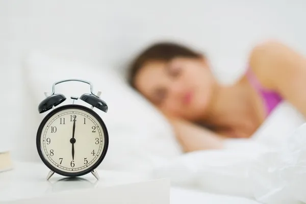 Alarm clock on table and woman sleeping in background Stock Picture