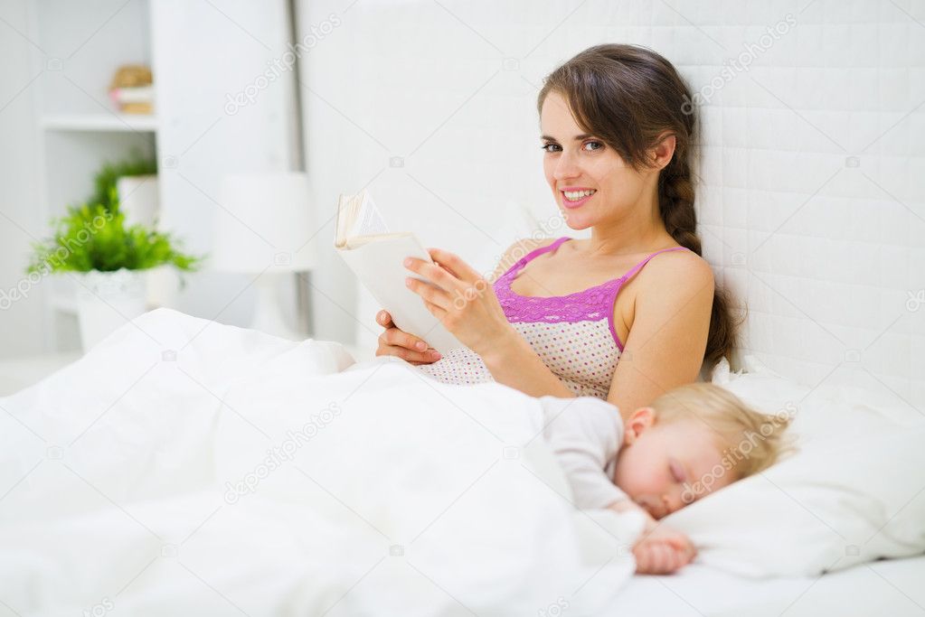 Mother reading in bed while baby
