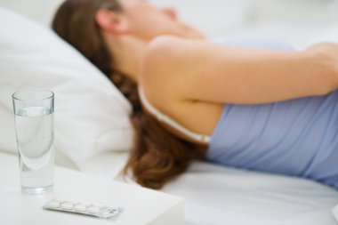 Closeup on pills and glass of water on table and sleeping girl i clipart