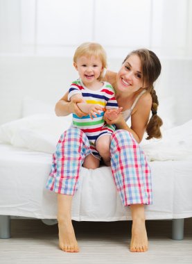 Portrait of smiling mother and baby in bedroom clipart