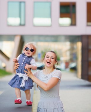 Smiling mother playing with baby in city clipart