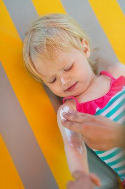 Baby waiting while mother applying sun block creme on arm clipart