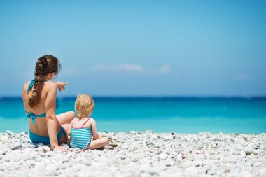 Mother sitting with baby on sea shore looking into distance. Rea clipart