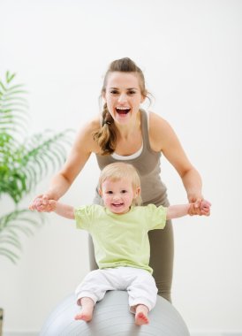 Mother mother holding baby sitting on fitness ball clipart