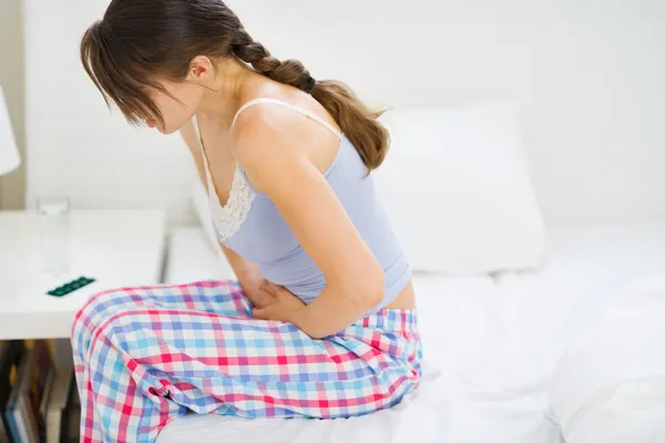 Meisje met buikpijn zittend op bed — Stockfoto