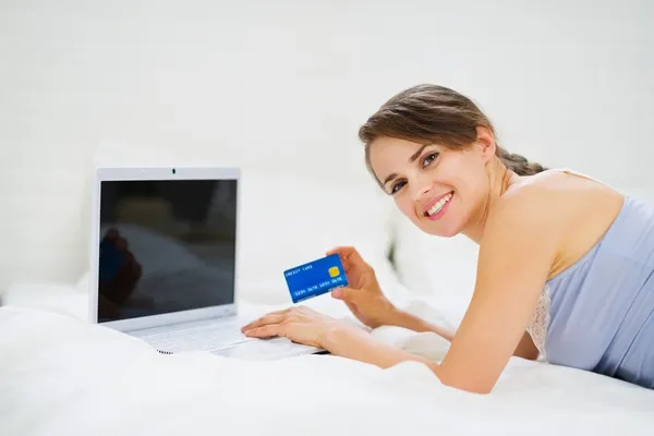 Улыбающаяся женщина лежит на кровати с ноутбуком и делает покупки в сети — стоковое фото