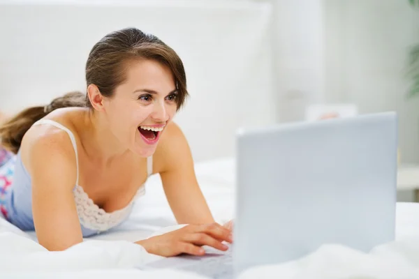 Frau liegt auf Bett und schaut überraschend in Laptop — Stockfoto