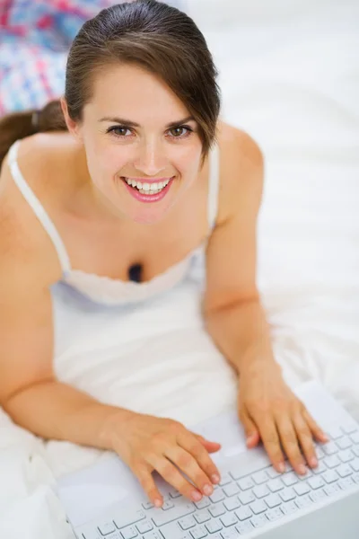Mujer sonriente acostada en la cama y trabajando en el portátil. Vista superior —  Fotos de Stock