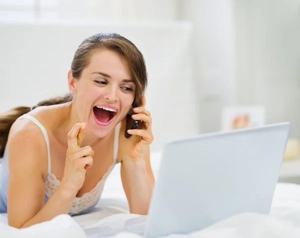 Excited woman with laptop speaking mobile with crossed fingers — Stock Photo, Image